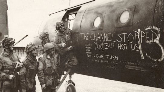 Paratroops in their war paint reading slogans chalked on a glider.