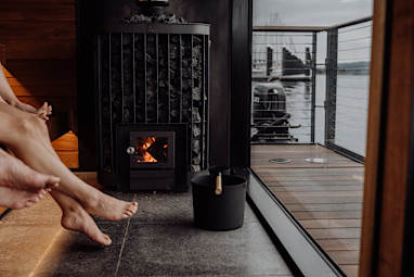 Feet of two people in a sauna, outside is a wooden deck and water