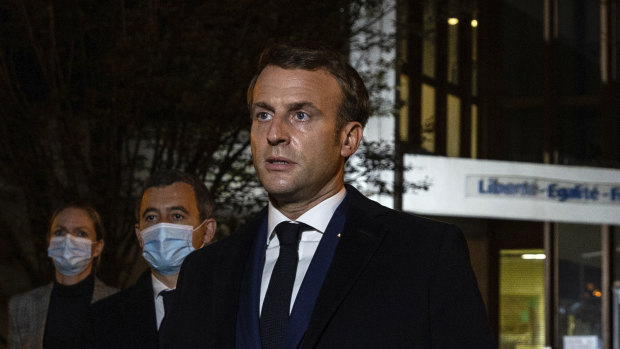 French President Emmanuel Macron, flanked by French Interior Minister Gerald Darmanin, second left, speaks in front of a high school northwest of Paris, after a history teacher was beheaded. 