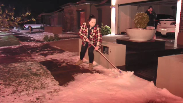 A woman sweeps hail from the footpath at Fraser Rise on Thursday evening. 