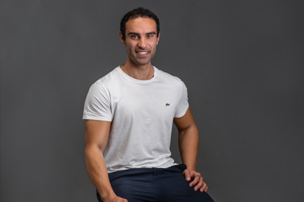 Biohacker Lucas Aoun poses for a headshot against a grey backdrop.