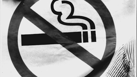 A man smokes in front of an Anti-Smoking sign.