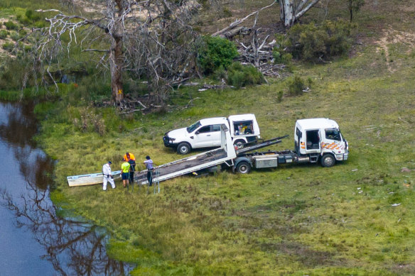 Police and a town truck remove a dinghy from a dam.