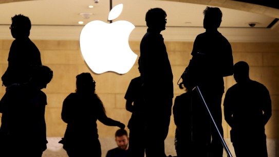 Customers stand beneath an Apple logo at the Apple store in New York.