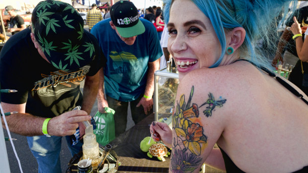 Bud tender Kansas, right, offers up a puff of cannabis concentrates at the Turtle Puddles' booth at the cannabis-themed Kushstock Festival at Adelanto, California.