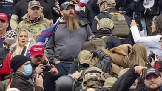 A line of men wearing helmets and body armour walk up the stairs outside the US Capitol on January 6 in single file, each man holding the jacket collar of the man ahead.