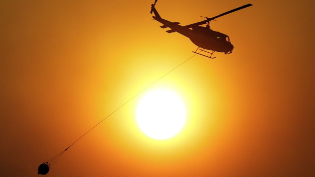 A helicopter carries water to drop on an advancing wildfire near Finley, California.