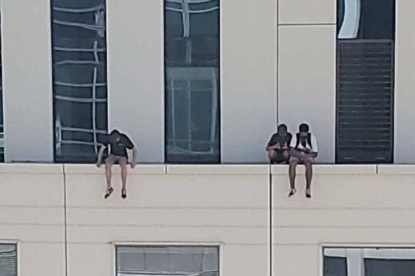 A group of young people sit with their legs dangling over the edge of a narrow ledge on the 12th floor of the Hyatt Regency Sydney hotel.