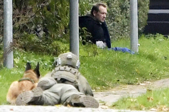 A police office watches Peter Madsen as he sits on the side of a road after being apprehended.