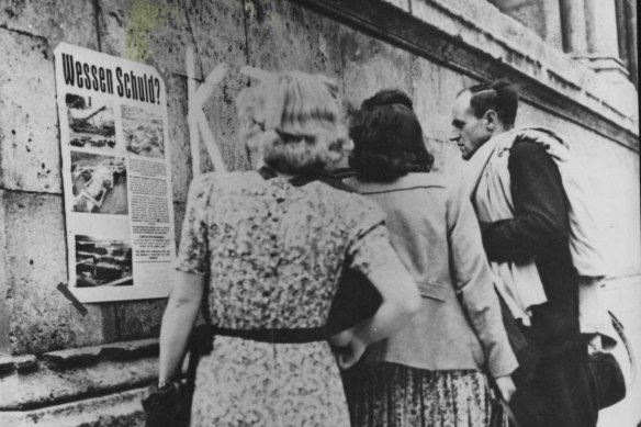 German civilians in Munich look at a poster displaying pictures of atrocities at Nazi death camps under the heading 'Whose guilt?'.
