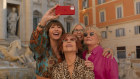 A film still of Mary Steenburgen, Jane Fonda, Diane Keaton and Candice Bergen, four immaculately dressed older women, pose in front of the Trevi fountain, Steenburgen holding her phone up.