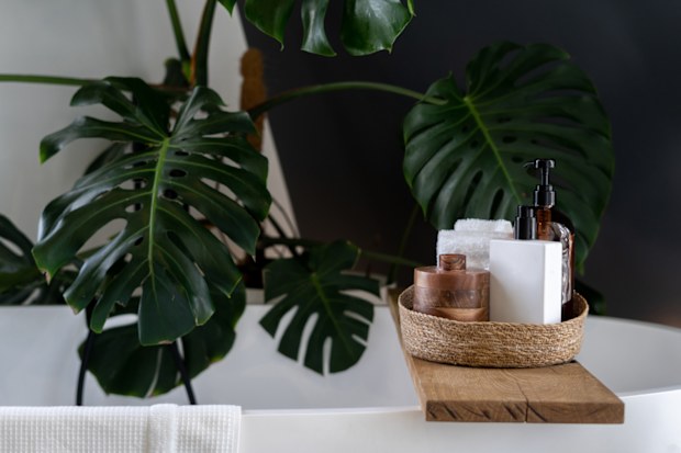 Wooden shelf for beauty and body care products at wooden shelf over modern white bathtub.