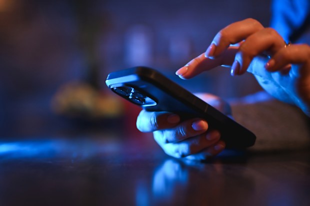 Woman's hands texting on a mobile phone with blue screen light in a dark room