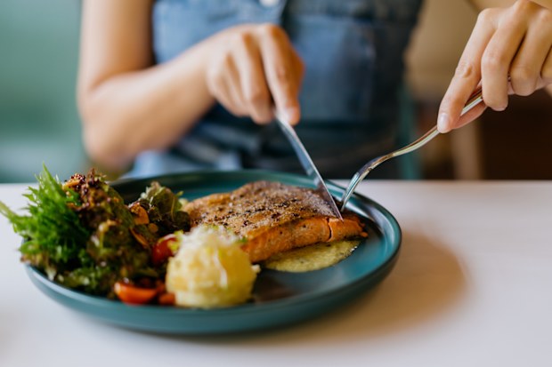 Stock image of a woman eating salmon and vegetables