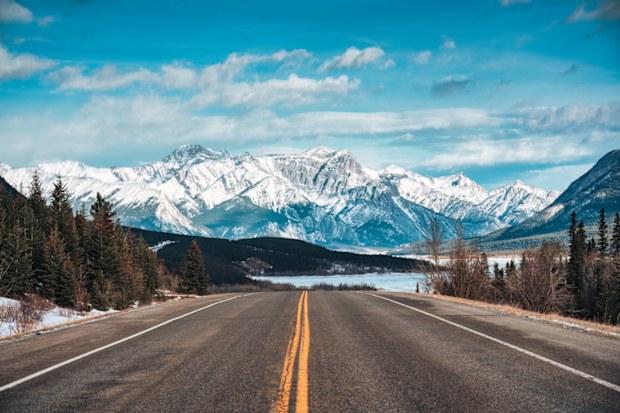 Road trip with car driving on highway road with snow covered rocky mountains in winter at Kootenay plains area, Alberta, Canada
