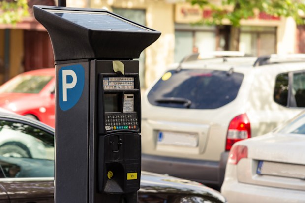 Parking meter with solar panel for alternative energy consumption next to a couple of cars in a parking lot
