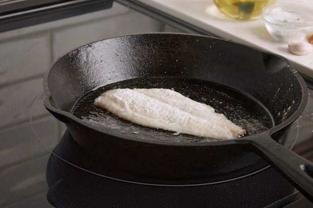 Cod fillet coated in flour frying in oil in cast iron pan. Step in seafood cooking preparation series.