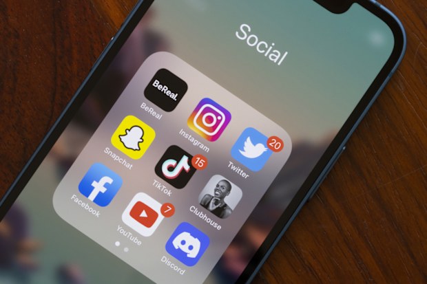 Assorted popular social media apps - BeReal, Instagram, Twitter, Snapchat, TikTok, Clubhouse, Facebook, YouTube, and Discord - are seen on an iPhone.
