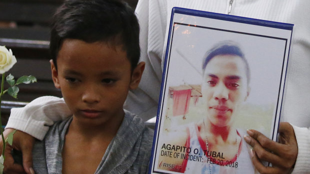 A boy stands next to his mother, who holds a portrait of his brother, an alleged victim of President Rodrigo Duterte's 'war on drugs', during a religious service in Manila in 2018.
