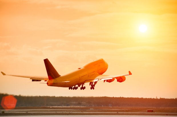 Airplane (Boeing 747-400) taking off at beautiful sunset, lens flare, orange sky, hot air evaporating from jet engines.