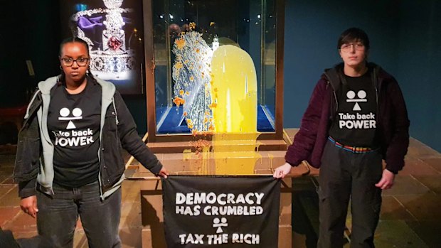 Take Back Power activists pose in front of a dessert-smeared Crown Jewels case at the Tower of London. The State Crown was not damaged during the custard and crumble incident.