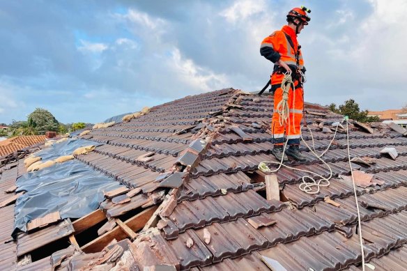 An SES member stands on a damaged roof in Cockburn after Tuesday nights damaging winds ripped off the tiling. 