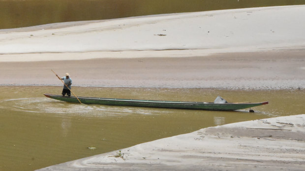 A man guides a traditional boat in shallow water on the Mekong River, on the Thai-Lao border. 