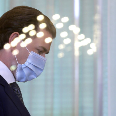 Austrian Chancellor Sebastian Kurz walks with a protective mask behind a reflective shield at the federal chancellery in Vienna.