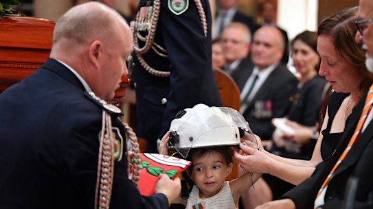 Charlotte O'Dwyer, the young daughter of Rural Fire Service volunteer Andrew O'Dwyer, with Andrew's wife Melissa, receiving her father's helmet after being presented with her fathers service medal by RFS Commissioner Shane Fitzsimmons.