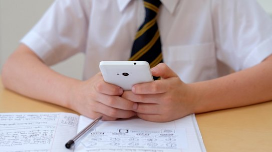 F1XTWB School pupil distracted by using a mobile phone (texting) whilst sat at his desk with his course work home work .