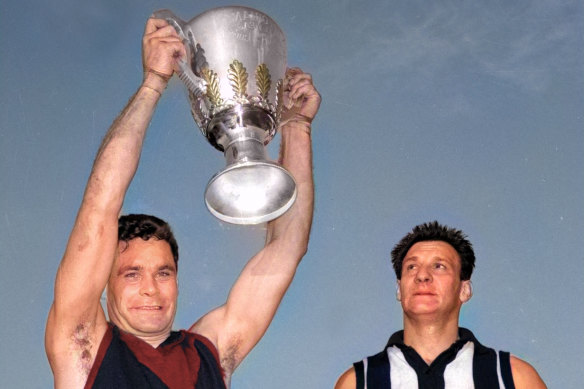 Melbourne captain Ron Barassi holds up the 1964 VFL premiership cup as Collingwood captain Ray Gabelich looks on.