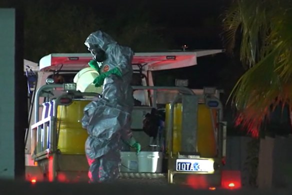 A polícia despeja produtos químicos em tambores em frente à casa do acusado. 