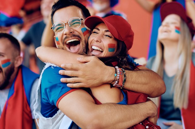 Cheerful couple having fun and embracing while spectating sports match from stadium stands.