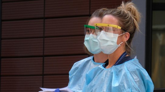 Hospital staff assist people waiting in line to be screened for COVID-19 outside the Royal Melbourne Hospital. Around 80 members of Victoria's health workforce have tested positive to coronavirus.