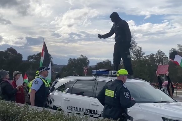 Federal officers confront a masked man atop a police car outside Parliament House.