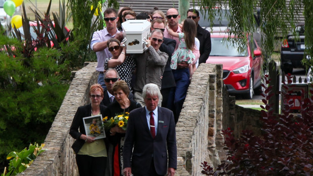 The Membrey family walk across the stone bridge at the Warrnambool Botanical Gardens, with the casket carrying Darcy Membrey.