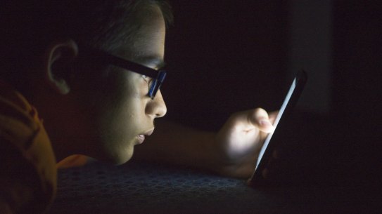 Teenager sending email from smart phone in his bed, Typing text message on smartphone. young cell phone addict teen  awake at night in bed using smartphone for chatting A smartphone offers unfettered access to the internet, so when should kids have one?