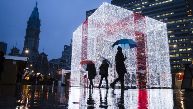 People walk on a rainy evening by The Present in the Christmas Village at John F. Kennedy Plaza, commonly known as Love Park, in Philadelphia, Thursday, Dec. 20, 2018. 
