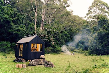 A small cabin in a clearing surrounded by bush