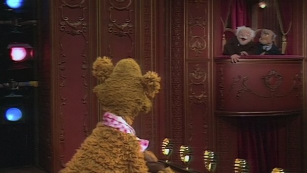 Statler and Waldorf heckle Fozzie Bear on stage in The Muppet Show.