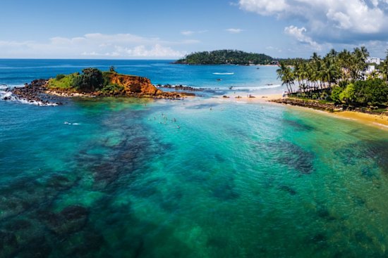 Aerial panorama of the tropical beach and clear sea with coral reefs in the town of Mirissa, Sri Lanka.