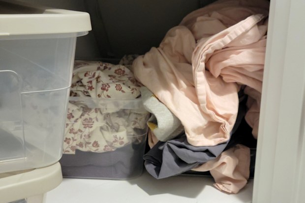 A photo of a linen closet overflowing with various linens, blankets, and storage containers.