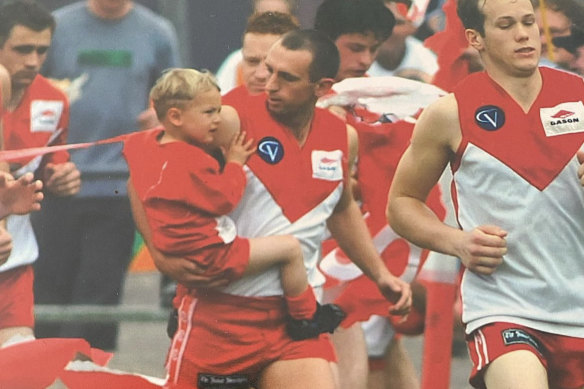 A three-year-old Tom Williamson is carried through the banner by his father Allister in 2001, the last time Ararat won a premiership.