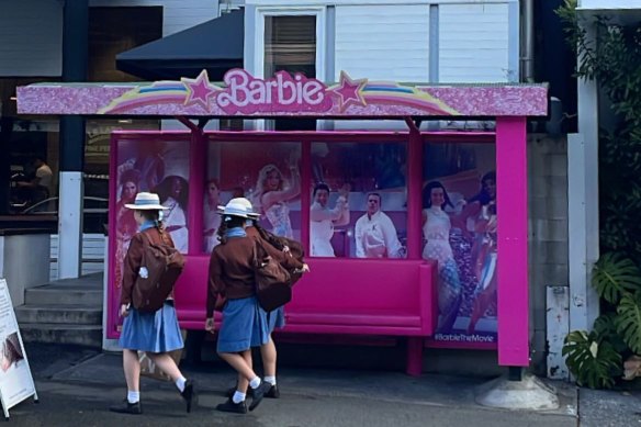 Schoolgirls walk past a Barbie-themed bus shelter on James Street in Fortitude Valley, Brisbane.