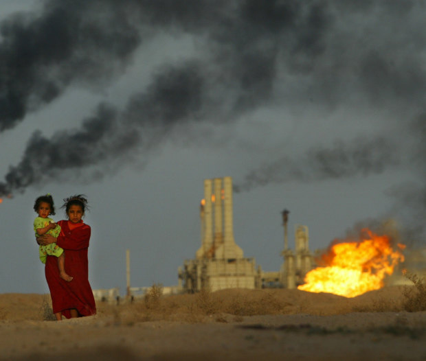 A young girl and her baby sister emerge from the heat and smoke from a petrochemical plant near their family farm, just north of the Iraq-Kuwait border. 