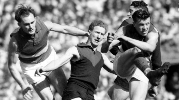 From the 1954 grand final: Bulldogs legend Ted Whitten clears the ball as Melbourne’s Stuart Spencer (centre) and Geoff McGivern (partially hidden) were unable to stop him. 