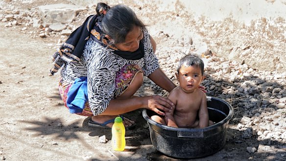 A mother bathes her daughter in a bucket after their home in Sembalun Bumbung was destroyed by the Lombok earthquake.