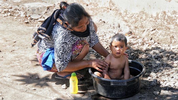 A mother bathes her daughter in a bucket after their home in Sembalun Bumbung was destroyed by the Lombok earthquake.