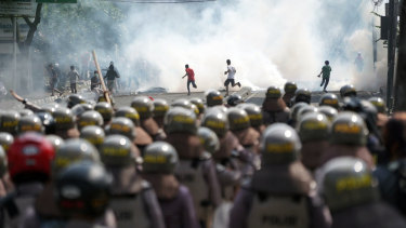 Police in riot gear, foreground, stand as demonstrators run from tear gas during a protest in Jakarta, Indonesia.