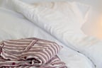 Striped pyjama shirt rests on a white bed with soft bedding and fairy lights in the background